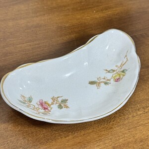 以下が含まれることがあります： 金色の縁と花のアクセントが付いた、白の腎臓型のセラミック皿。 ピンクと黄色のバラと緑の葉が特徴です。 この皿はおそらくヴィンテージまたはアンティークです。
