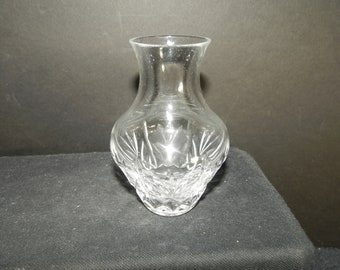 Puede incluir: Un florero de vidrio transparente con cuerpo bulboso y cuello acampanado. La parte inferior del florero está decorada con un patrón de vidrio tallado que consiste en líneas verticales y formas de diamante que captan la luz.