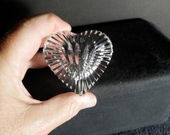 May include: A clear, heart-shaped glass object featuring deep, vertical radial cuts that create a faceted, light-reflecting surface. The piece has a pointed base and a rounded top, with a transparent, colorless appearance and a polished finish.