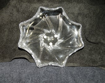 May include: A clear glass bowl featuring a six-pointed star shape with a swirling, ribbed pattern radiating from the center. The bowl has a smooth, transparent finish and a scalloped edge, creating a distinct geometric design that catches the light.