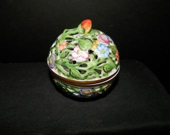 May include: A spherical ceramic lidded jar featuring an intricate openwork lattice design. The surface is decorated with hand-painted green leaves and colorful flowers in shades of pink, blue, and purple. An orange bud sits atop the lid.