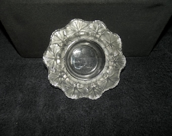 May include: A clear glass bowl featuring a decorative border of frosted, raised leaf motifs arranged in a circular pattern. The center of the bowl is smooth and transparent, while the outer rim displays detailed, textured foliage designs.