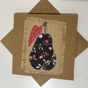 May include: A handmade greeting card with a pear design. The pear is made of black fabric with white polka dots and floral patterns, with red dotted leaves. The pear is on a burlap square, set on a brown card.