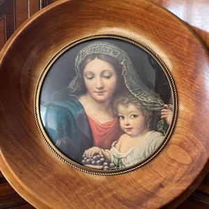 Puede incluir: Una pintura enmarcada de una mujer y un niño. La mujer lleva un vestido azul y rojo y un velo blanco. El niño sostiene un racimo de uvas. La pintura está enmarcada en un marco de madera.