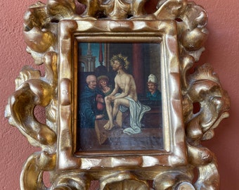 Puede incluir: Una pintura al óleo enmarcada que representa una escena de la Pasión de Cristo. La pintura muestra a Jesucristo, con una corona de espinas, sentado en una piedra con dos figuras de pie a su lado. La pintura está enmarcada en un marco dorado y ornamentado.