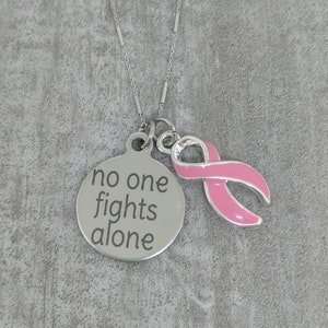 May include: A silver necklace with a pink ribbon charm and a round pendant that says "no one fights alone".