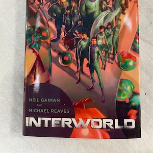 Op de afbeelding: Een boekomslag met een kleurrijke illustratie van een groep mensen in groene en paarse kleding. De titel "INTERWORLD" is gedrukt in grote witte letters op een donkerpaarse achtergrond.