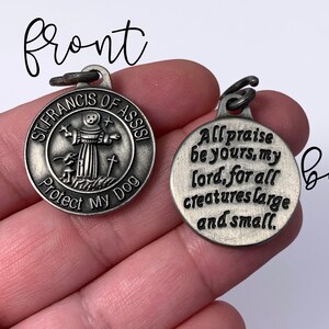 May include: A silver metal dog tag with a picture of Saint Francis of Assisi on the front and the text "ST. FRANCIS OF ASSISI Protect My Dog" and the text "All praise be yours, my lord, for all creatures large and small." on the back.