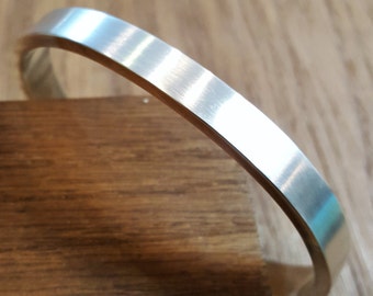 May include: A silver bracelet with a smooth, polished finish. The bracelet is made of a single, continuous piece of metal and has a simple, modern design.