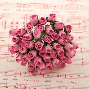 Puede incluir: Un ramo de pequeñas rosas de papel rosa, dispuestas en un ramo. Las rosas están agrupadas y tienen un aspecto delicado y realista.