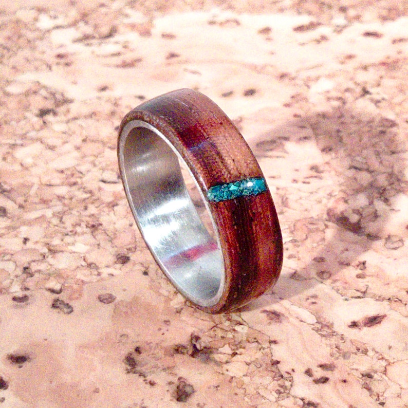 May include: A wooden ring with a silver band and a turquoise inlay. The ring is made of dark wood and has a natural finish.
