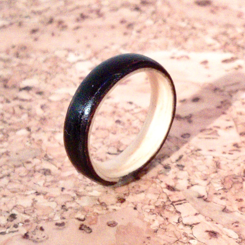 May include: A black and white wooden ring with a smooth, polished finish. The ring is made of two different types of wood, one dark and one light.