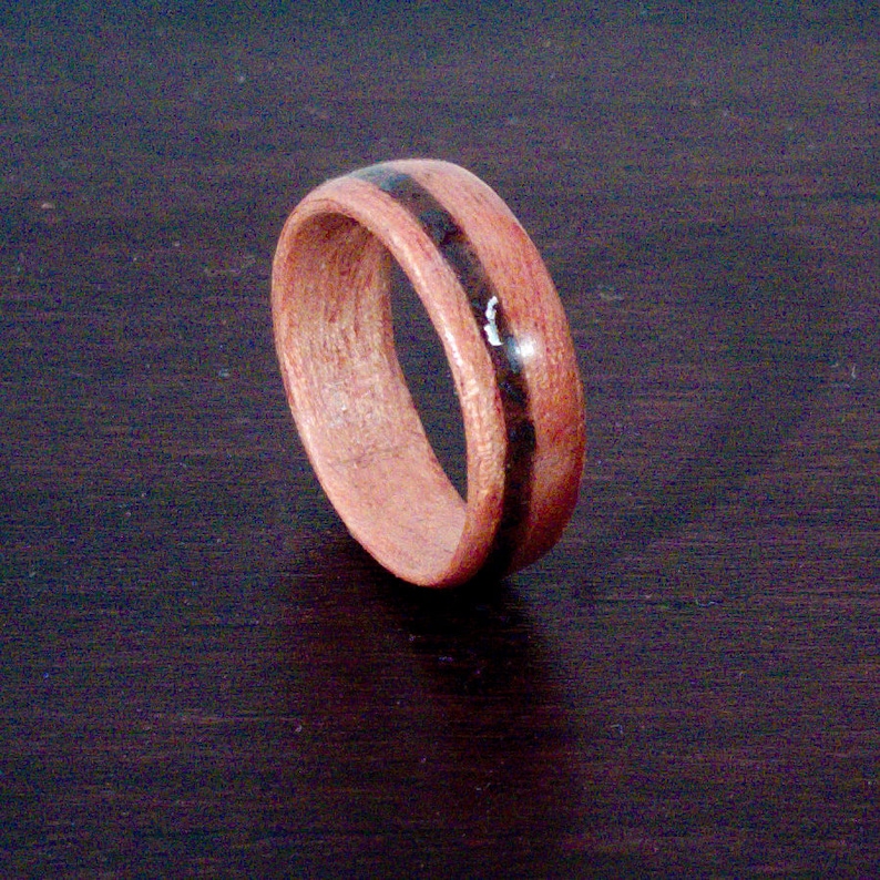 Op de afbeelding: Een houten ring met een zwarte inlay. De ring is gemaakt van lichtbruin hout en heeft een gladde afwerking.
