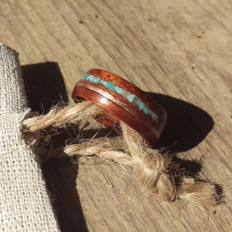 May include: A wooden ring with a thin copper band and a turquoise inlay. The ring is on a piece of twine.