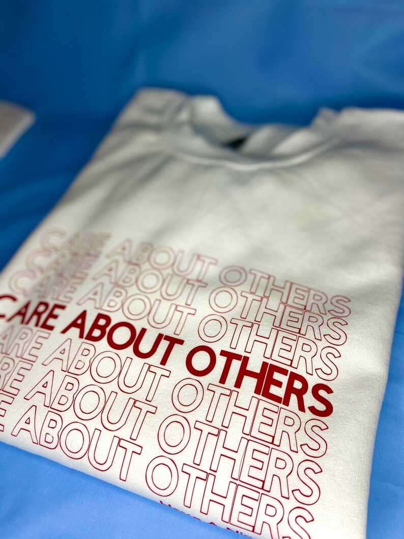 May include: White sweatshirt with the phrase "CARE ABOUT OTHERS" repeated in red lettering.
