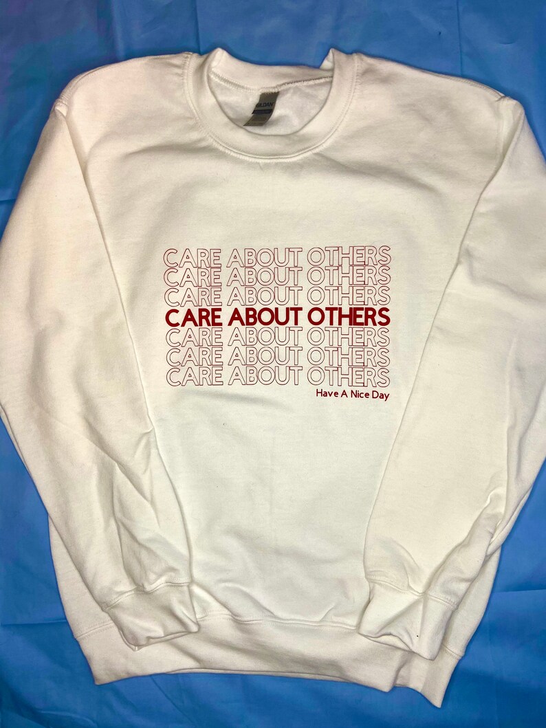 May include: A white sweatshirt with the phrase "CARE ABOUT OTHERS" repeated multiple times in red lettering. The text "Have A Nice Day" is printed in smaller red lettering below the repeated phrase.