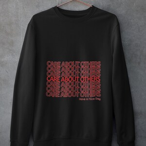 May include: Black sweatshirt with the phrase "CARE ABOUT OTHERS" repeated multiple times in red text. The text is stacked vertically and the phrase "Have A Nice Day" appears below the repeated phrase.