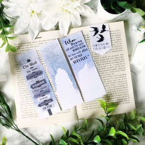 Puede incluir: Un conjunto de cuatro marcapáginas con citas e ilustraciones de la popular serie de fantasía Game of Thrones. Los marcapáginas están impresos en cartulina blanca con tinta azul y negra. Las citas incluyen "Se acerca el invierno", "Cuando el lobo joven y los vientos blancos soplan, el lobo solitario muere, pero la manada sobrevive." y "Madre de Dragones".