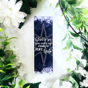 May include: A dark blue bookmark with a white star and the text "Glad to see you woke up ready to PLAY. Nesta."
