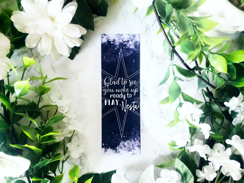 May include: A dark blue bookmark with a white star and the text "Glad to see you woke up ready to PLAY. Nesta."