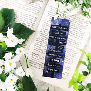 May include: A blue and purple bookmark with a starry background and a black sign that reads "Night Court Velaris Court of Nightmares" with arrows pointing to other courts: "Spring Court", "Autumn Court", "The Wall", "Summer Court", "Winter Court", "Dawn Court", and "Day Court".
