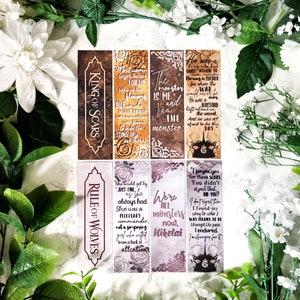 Puede incluir: Seis marcapáginas diferentes con citas de los libros "King of Scars" y "Rule of Wolves". Los marcapáginas están impresos en papel con un aspecto desgastado y vintage. Las citas están en texto marrón, blanco y negro.