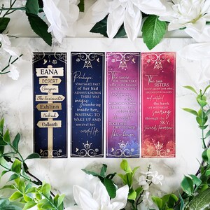 May include: Four colorful bookmarks with gold accents and a fantasy theme. Each bookmark features a different design with text that reads "Eana Desert", "Perhaps", "The Twins", and "The Two Sisters".
