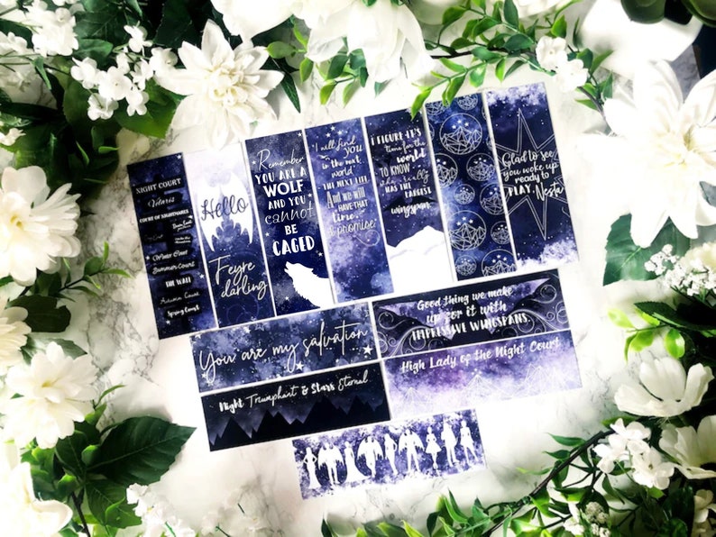 May include: A set of eight blue and white bookmarks with quotes from the book A Court of Thorns and Roses. The bookmarks feature a starry night sky background with silver glitter accents. The quotes include "Remember you are a wolf and you cannot be caged", "Hello Feyre darling", "You are my salvation", "Good thing we make up for it with impressive wingspans", "High Lady of the Night Court", "I figure it's time for the world to know", "Glad to see you woke up ready to play, Nesta", and "Night Court:  Courts of Tollenmere".