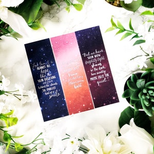 May include: Four rectangular bookmarks with inspirational quotes. The bookmarks have a gradient background of blue, pink, and purple with white text. The bookmarks are surrounded by white flowers and greenery.