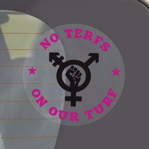 May include: A clear car window sticker with the text "NO TERFS ON OUR TURF" in pink, encircling a black symbol of gender identity and a raised fist. Two pink stars are also included in the design.