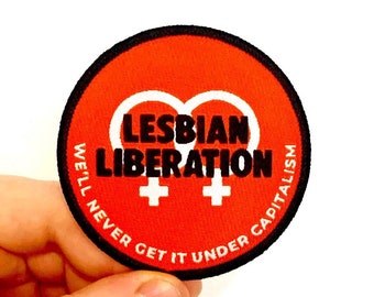 May include: Red and black embroidered patch with the text "Lesbian Liberation" and two white female symbols. The text around the symbols reads "We'll never get it under capitalism."