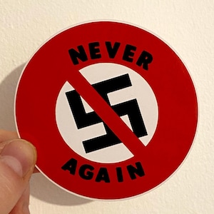 Könnte beinhalten: Ein roter Kreisaufkleber mit dem Wort "NEVER" über einem schwarzen Hakenkreuz mit einem diagonalen roten Strich durch ihn. Das Wort "AGAIN" befindet sich unter dem Hakenkreuz.