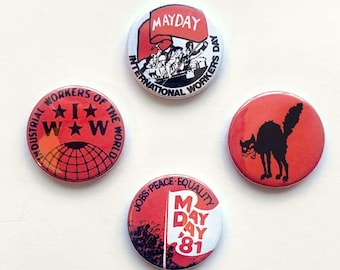 May include: Four red, white, and black button badges with different designs. The first badge says "Industrial Workers of the World" with a star and the letters "IWW". The second badge says "Mayday International Workers Day" with a red flag and a group of people. The third badge has a black cat with a red background. The fourth badge says "Jobs Peace-Equality Mayday 81" with a red flag.