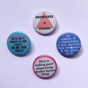 Peut inclure: Quatre boutons ronds avec des messages différents. Le premier bouton est bleu avec un triangle arc-en-ciel et le texte "We're not a danger to your family. We are your family!" Le deuxième bouton est blanc avec un triangle rose et le texte "Knowledge = Change". Le troisième bouton est bleu avec le texte "The quality of a relationship is more important than the gender of the people in it". Le quatrième bouton est rose avec le texte "There is nothing queer about loving another human being."