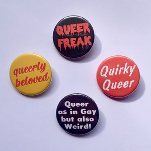 May include: Four round black, yellow, red, and black buttons with white text. The buttons read "Queer Freak", "queerly beloved", "Quirky Queer", and "Queer as in Gay but also Weird!"