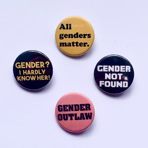 May include: Four round buttons with different messages about gender identity. The buttons are black, pink, and yellow with black text. The text on the buttons reads: "Gender? I hardly know her!" "All genders matter." "Gender Outlaw" and "Gender Not Found."