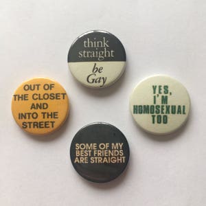 Peut inclure: Quatre boutons ronds avec des messages différents sur le fait d'être gay. Les boutons sont jaunes, noirs, blancs et crème. Le texte sur les boutons est : "Out of the closet and into the street", "Think straight be gay", "Some of my best friends are straight", et "Yes, I'm homosexual too".