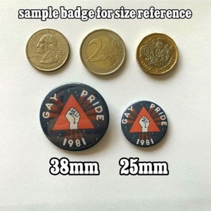 Peut inclure: Deux badges ronds &laquo; Gay Pride &raquo; de 38 mm et 25 mm, avec un poing dans un triangle rouge, entour&eacute;s de texte. Les badges sont &agrave; c&ocirc;t&eacute; d'un quart de dollar am&eacute;ricain, d'une pi&egrave;ce de 2 euros et d'une pi&egrave;ce d'une livre britannique.