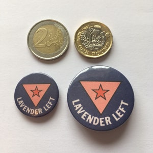 May include: Two button badges with the text "Lavender Left" in white lettering on a dark blue background. A pink triangle with a red star inside is centered on each badge. The larger badge is 1.5 inches in diameter and the smaller badge is 1 inch in diameter.
