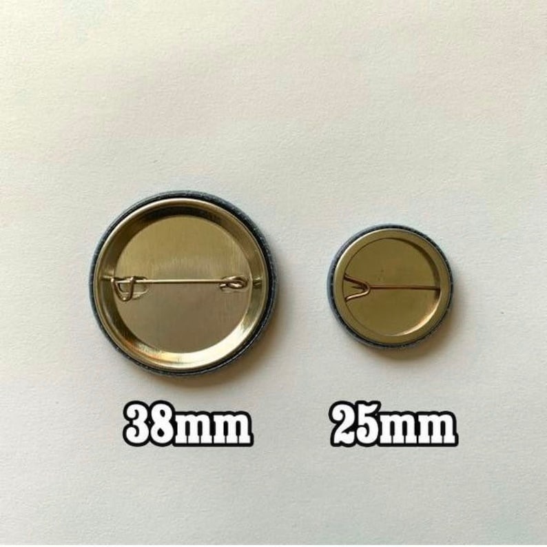 Peut inclure: Deux badges ronds avec des dos en m&eacute;tal. Le plus grand mesure 38 mm de diam&egrave;tre, et le plus petit 25 mm. Les deux badges ont une &eacute;pingle de s&ucirc;ret&eacute; &agrave; l'arri&egrave;re. Les badges sont sur un fond clair.
