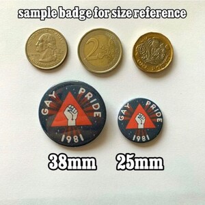 Puede incluir: Dos botones redondos con pin, con fondo negro y un tri&aacute;ngulo rojo con un pu&ntilde;o blanco en el centro. El texto "Gay Pride 1981" est&aacute; impreso en blanco alrededor del tri&aacute;ngulo. El bot&oacute;n m&aacute;s grande tiene 38 mm de di&aacute;metro y el m&aacute;s peque&ntilde;o 25 mm de di&aacute;metro.