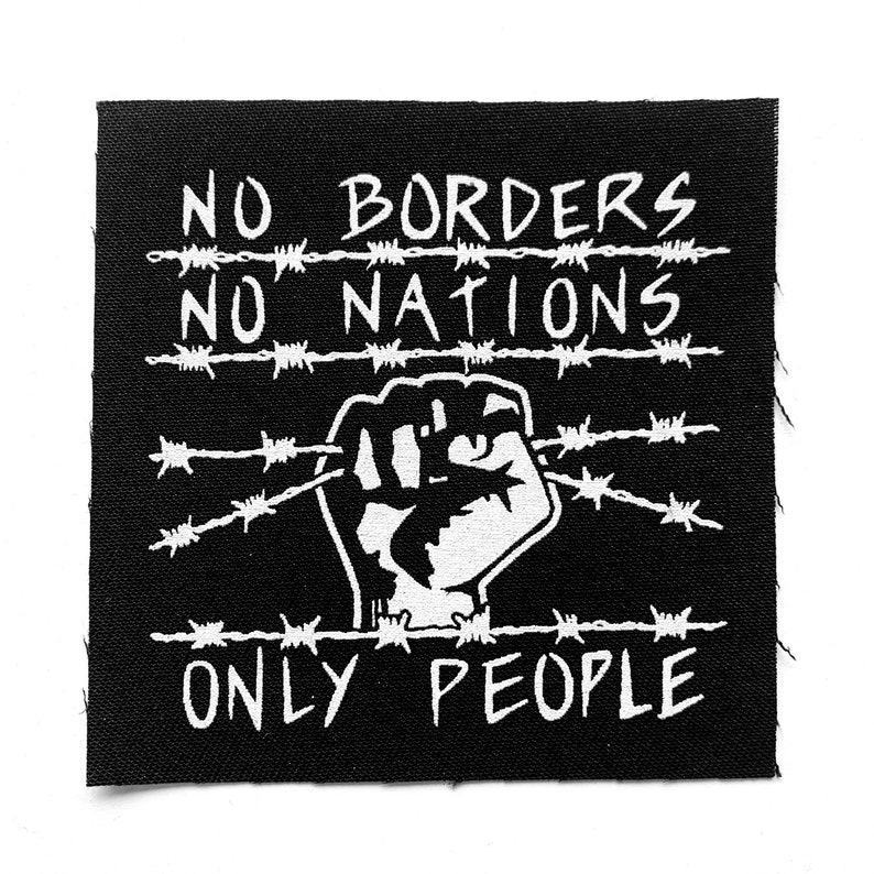 May include: Black square patch with white text and graphic. The text reads "NO BORDERS NO NATIONS ONLY PEOPLE." A clenched fist graphic is in the center, with barbed wire lines above and below the fist.