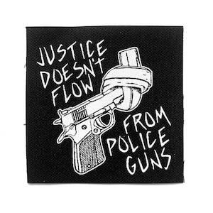 May include: Black and white patch with a gun tied in a knot. The text reads "Justice Doesn't Flow From Police Guns".