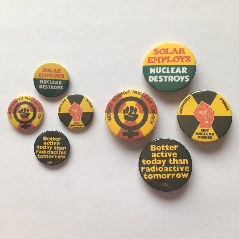 Pu&ograve; includere: Una collezione di otto bottoni rotondi con vari slogan e grafiche relative all'energia nucleare. I bottoni sono gialli, verdi, neri e rossi con testo nero. Gli slogan includono "Solar Employs Nuclear Destroys", "Women Against Nuclear Energy", "Not Nuclear Power", e "Better Active Today Than Radioactive Tomorrow".
