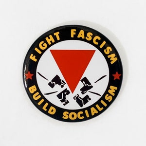 May include: Black and yellow button with the text "Fight Fascism Build Socialism" in a circle around a red triangle with black fists breaking through it.