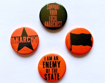 May include: Four round orange and black buttons with political slogans. The buttons read "Support Your Local Anarchist", "Anarchy", "I Am An Enemy Of The State", and a black flag on an orange background.