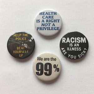 Op de afbeelding: Vier ronde button badges met verschillende berichten. De eerste badge is wit met blauwe tekst die "Health Care Is A Right Not A Privilege" luidt. De tweede badge is zwart met witte tekst die "Help The Police Beat Yourself Up" luidt. De derde badge is wit met zwarte tekst die "We Are The 99%" luidt. De vierde badge is zwart met witte tekst die "Racism Is An Illness Are You Sick?" luidt.