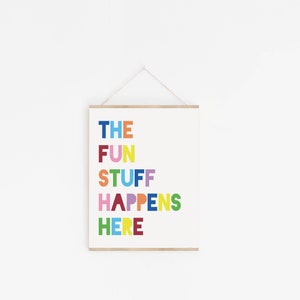 Może przedstawiać: Biały plakat z tekstem "THE FUN STUFF HAPPENS HERE" w kolorowych literach. Plakat wisi na białej ścianie.