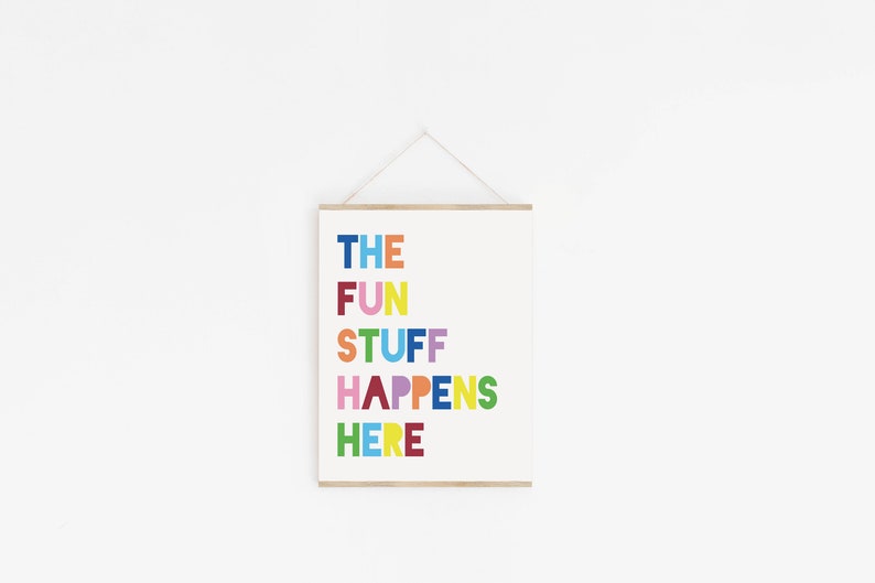 Może przedstawiać: Biały plakat z tekstem "THE FUN STUFF HAPPENS HERE" w kolorowych literach. Plakat wisi na białej ścianie.