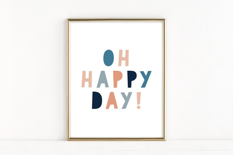 May include: A framed art print with the words "OH HAPPY DAY!" in a playful, colorful font. The text is in shades of blue, peach, and gray against a white background, framed in gold.